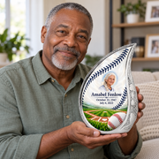 An adult holding the Curved Drop baseball memorial urn, with its personalized artwork visible.
