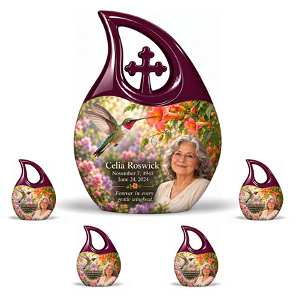 Hummingbird 01 Cross Drop, 10 inch large Urn with 4 Keepsake 3 Inch Urns: glossy mulberry-plum loop above a ruby-throated hummingbird, coral trumpet flowers and rose-lavender garden; fictional Celia Roswick portrait, name and full dates.