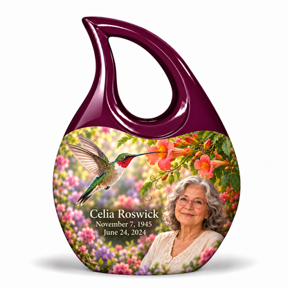 Hummingbird 01 Cross Drop, 1 Keepsake 3 inch Urn: glossy mulberry-plum loop above a ruby-throated hummingbird, coral trumpet flowers and rose-lavender garden; fictional Celia Roswick portrait, name and full dates.