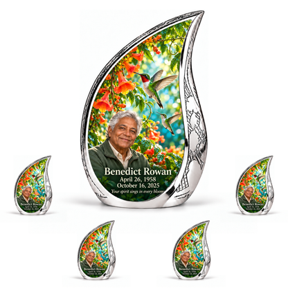 Hummingbird 01 Curved Drop, 10 inch large Urn with 4 Keepsake 3 Inch Urns: engraved silver Curved Drop surrounding two hummingbirds, orange trumpet vine and turquoise garden; fictional Benedict Rowan portrait, name and full dates.