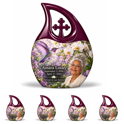 Hummingbird 02 Cross Drop, one large urn with four identical keepsakes: violet hummingbird and white orchids, solid plum large cross loop and four no-cross open loops; Amara Loxley portrait, name and full dates on a white backdrop.