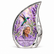 Silver Curved Drop urn with engraved rim and sidewall, emerald-violet hummingbird among lavender and Meera Hollingford portrait, name and full dates.