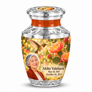 One Tasty keepsake with flat silver lid and central golden-bird art inset, orange neck, cactus blooms and Akiko Valehurst portrait and full dates.