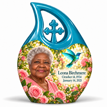 10 inch large Urn; Glossy turquoise Cross Drop with vivid turquoise/cyan hummingbird wings and soft pink roses. Corrected Leona Birchmere has a broad hexagonal face, strong wide jaw, broad flat nose, low brows, round widely spaced eyes, full wide lips, short silver natural curls and pink blouse. Dark teal name and October 14, 1934 / January 14, 2021 dates are accurate.